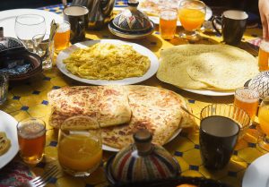 Table full of Moroccan breakfast with msemen, beghrir, omelette, Moroccan tea, and fresh orange juice at Nomad Surf Camp